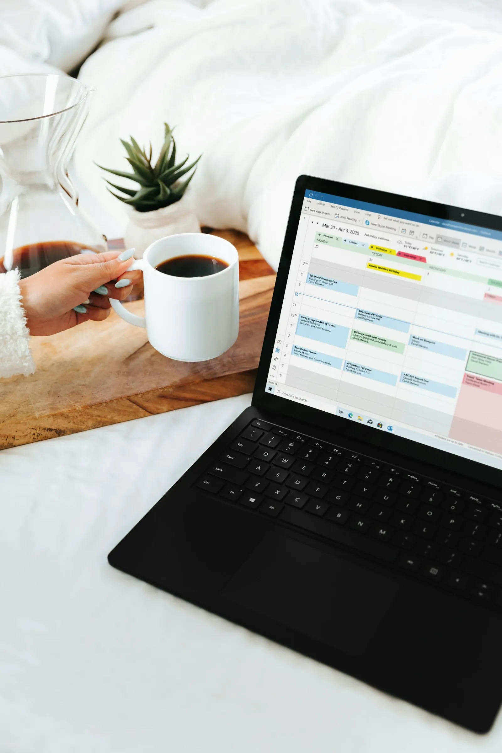 A laptop showing a week of colour-coded appointment slots, beside a coffee
