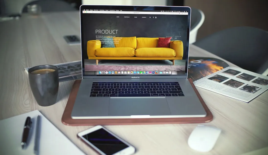 A laptop on a desk showing a website, with a phone and printed work beside it