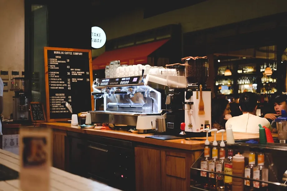 An espresso bar with cups on the machine and a customer waiting at the counter