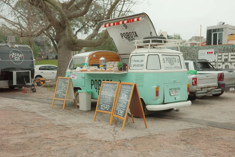 A food truck parked on a street with its service window open and customers queuing