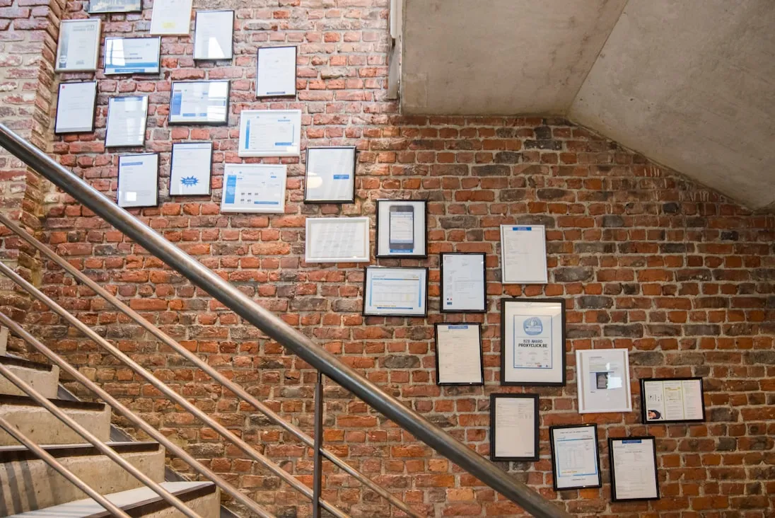 A stairwell wall hung with dozens of framed licences and certificates